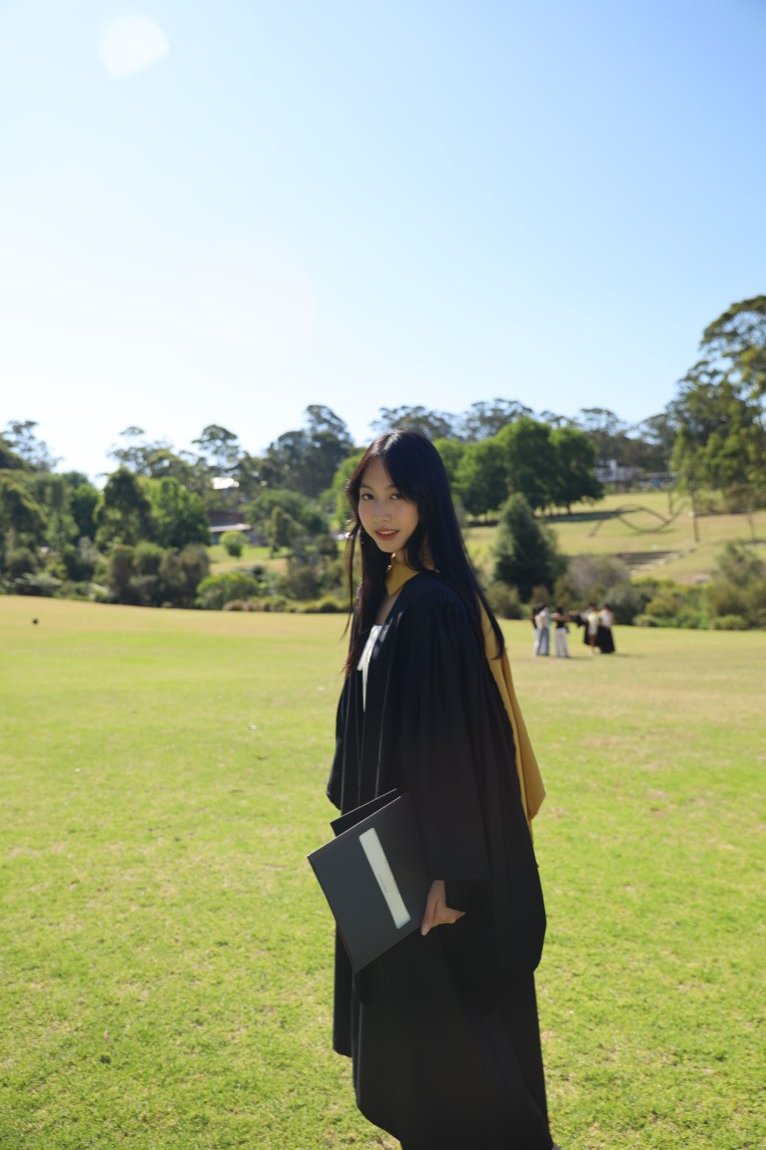 Graduate looking back over her shoulder on a wide green lawn