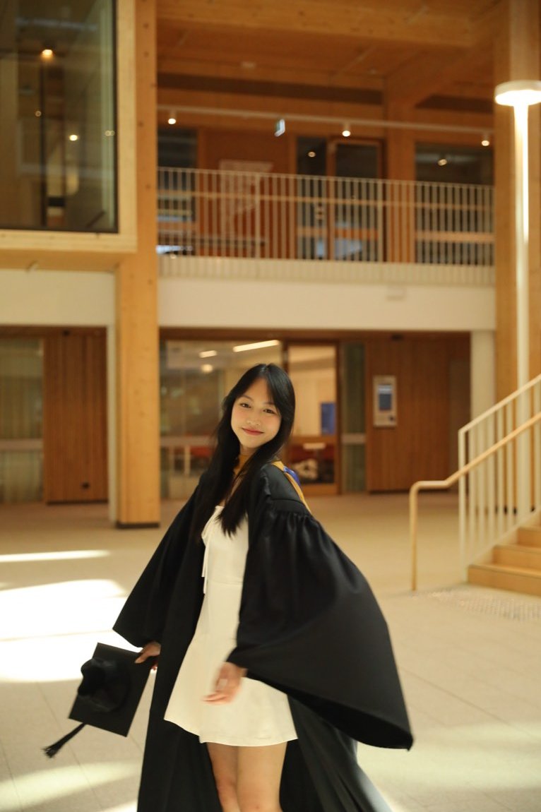 Graduate swishing her gown in a timber atrium