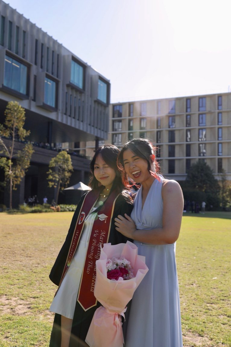 Graduate hugged by a laughing friend in a blue dress