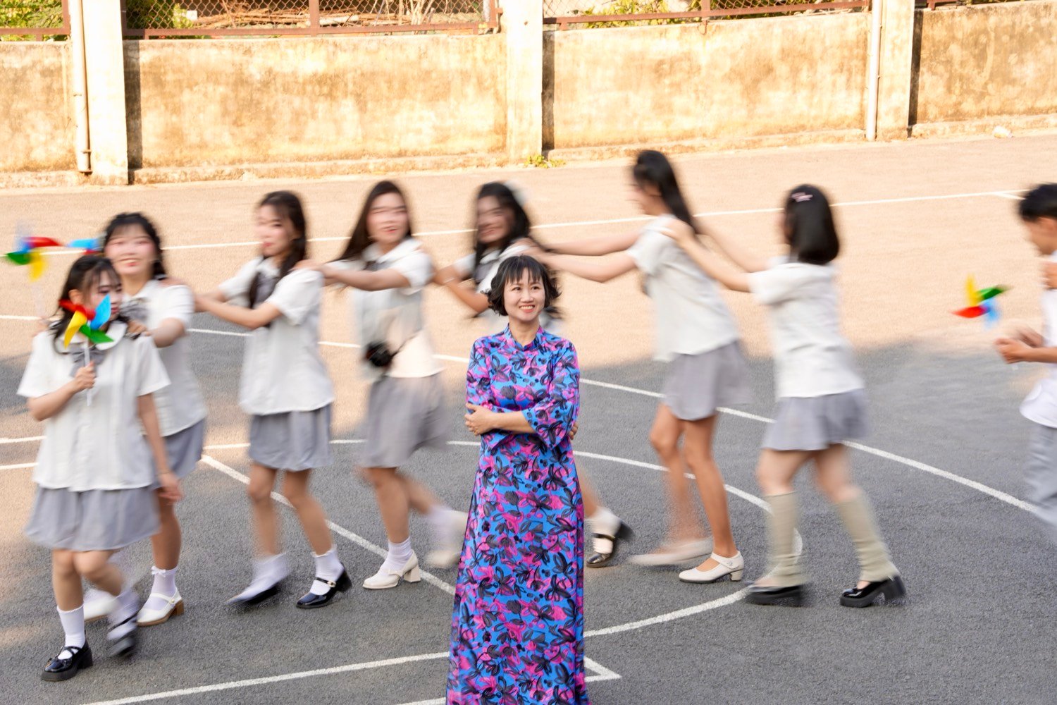 Teacher sharp and smiling while students blur in a ring around her
