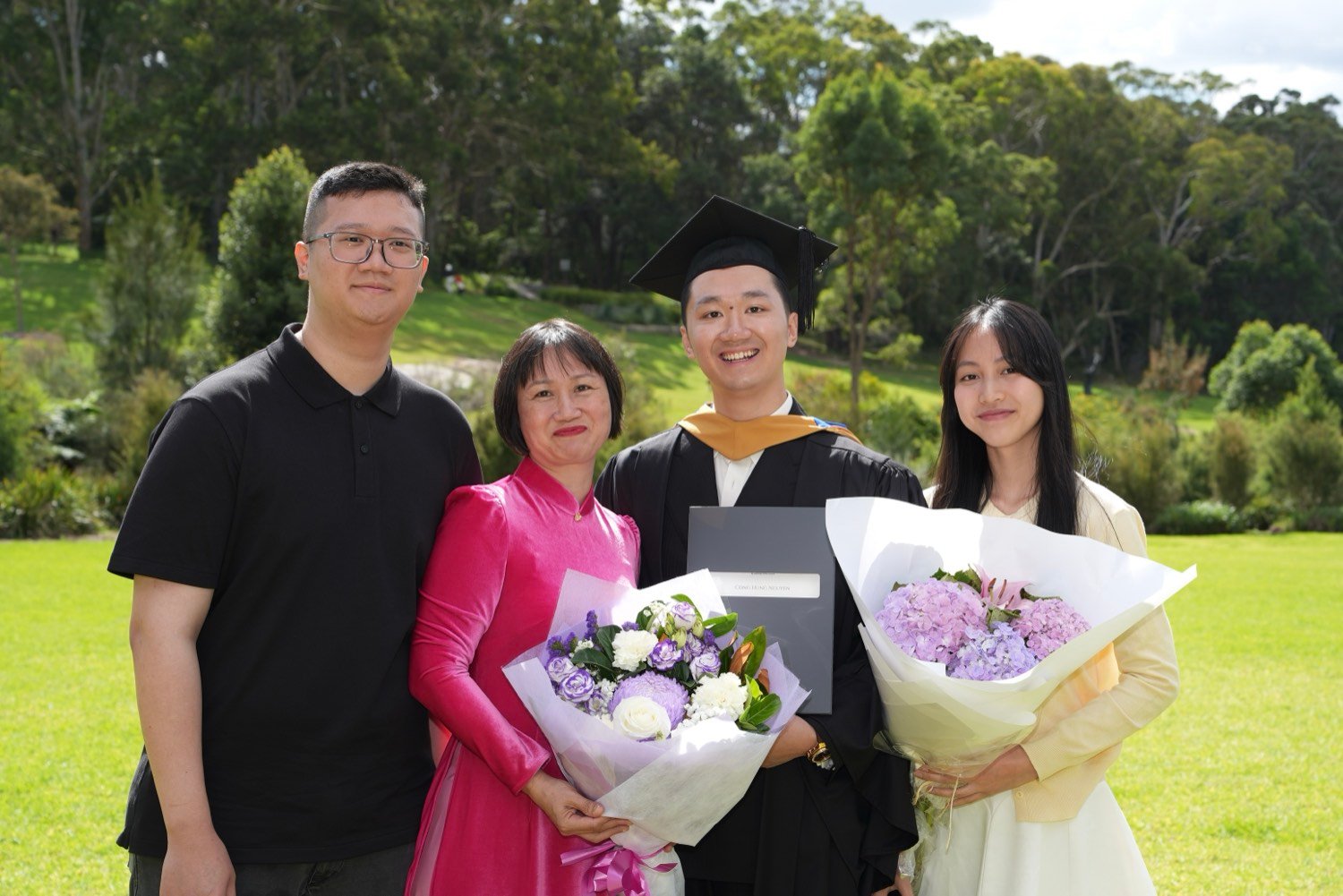 Graduate with his family holding flowers on a sunlit lawn