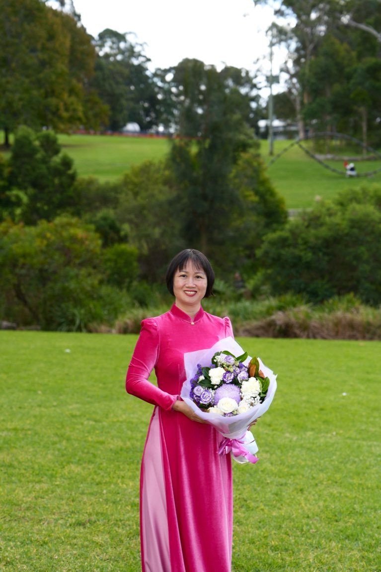 Mother in pink ao dai with a bouquet against greenery