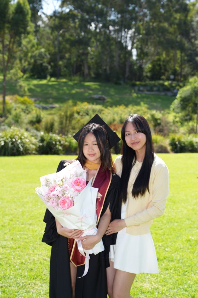 Graduate with pink roses embraced by her sister