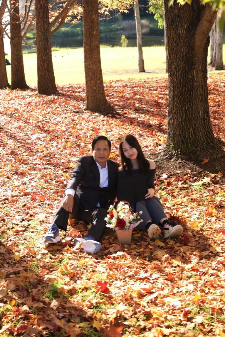 Father and daughter seated among golden fallen leaves