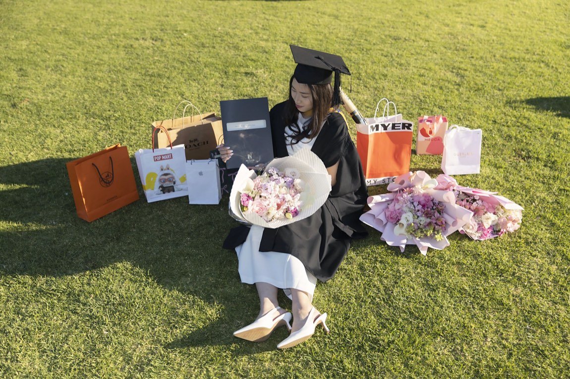 Graduate seated on the lawn among gift bags and bouquets